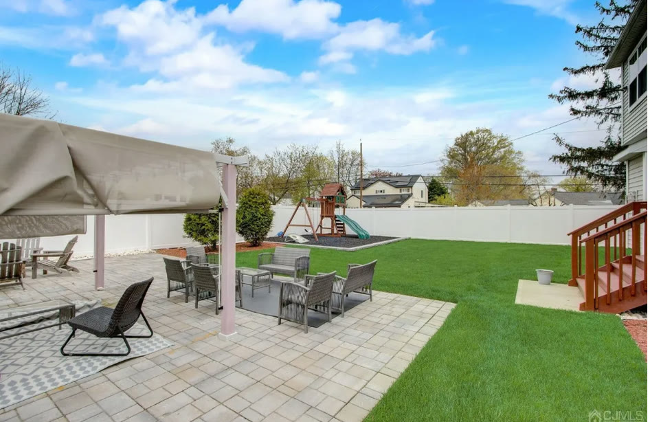 Paver patio with lounge seating looking across the lawn to the playset
